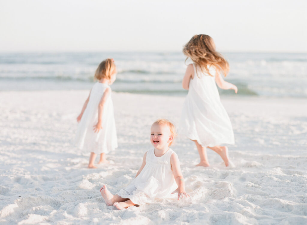 Three sisters twirl on the beach in 30A in their white dresses while 30a photographer Kaylie B. Poplin photography takes their family photos. 