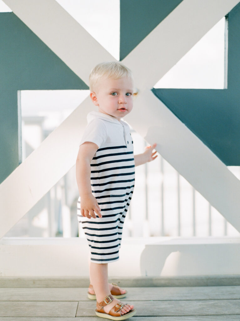 A little boy in a navy and white striped romper stands at the top of the Seaside pavilion. 