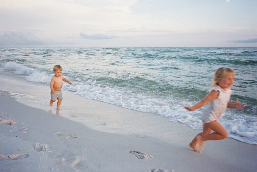 A little girl and little boy race by the seaside in their swimsuits in Panama City Beach, Florida.