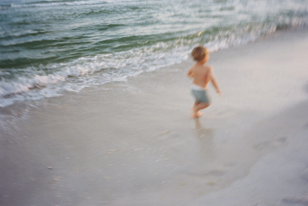 A little boy with blonde hair runs as fast as he can along the beach in Panama City Beach, Florida.