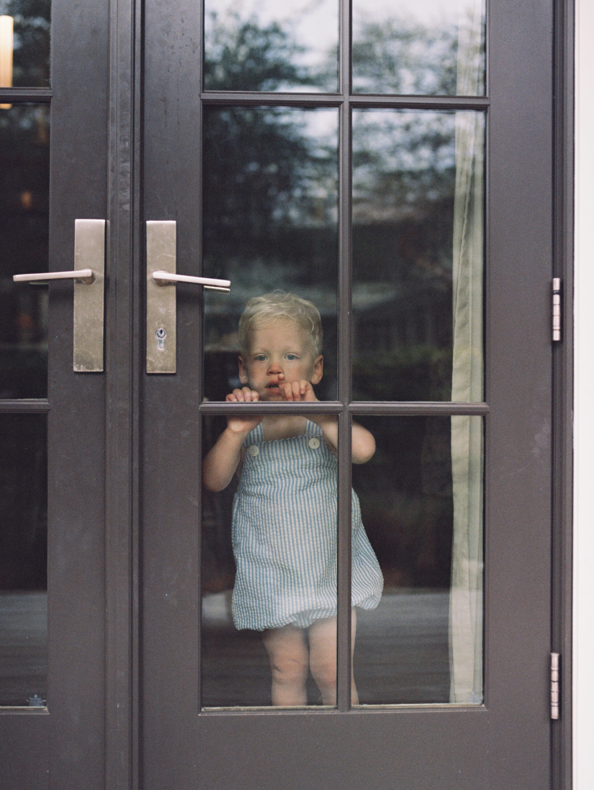 A little boy with blonde hair and blue eyes peeking out the front door.