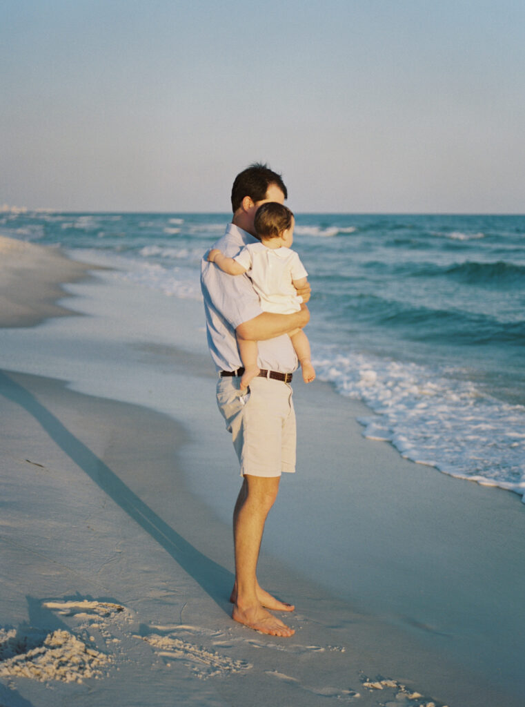 A father holds his son on the beach in 30A while watching the waves roll in.