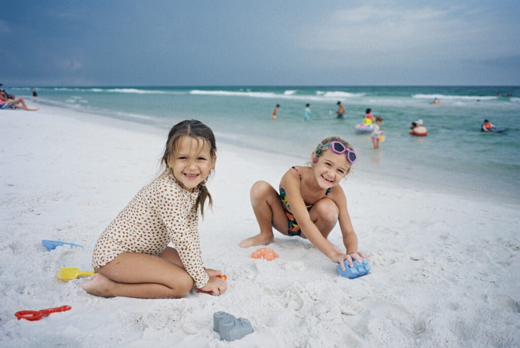 Two little girls play with sand toys on the beach in their swimsuits at Topsail Hill Preserve State Park.