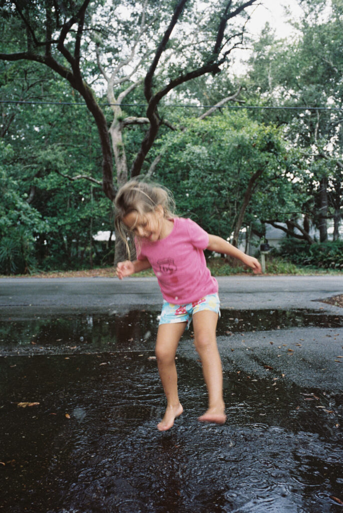 A little girl with her hair back in a braid jumps in a rain puddle in her driveway in Shalimar, Florida.