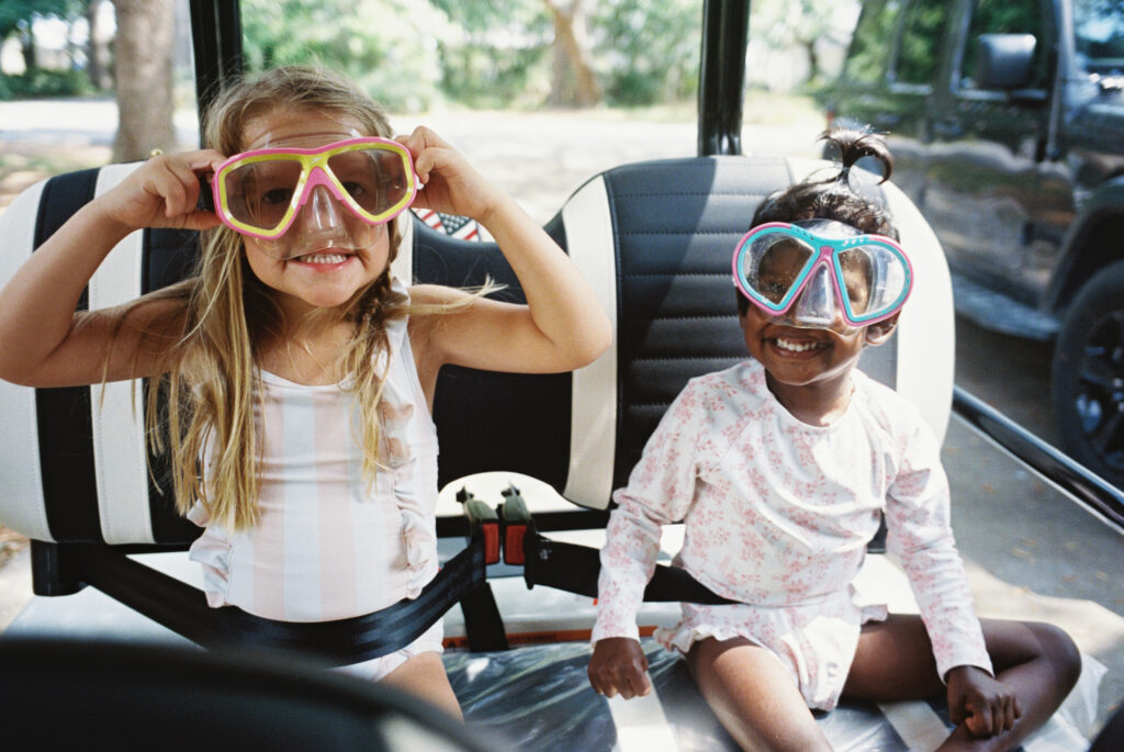 Two little girls wear beach googles on their face while waiting patiently on their golf cart to go to the beach in Shalimar, Florida.