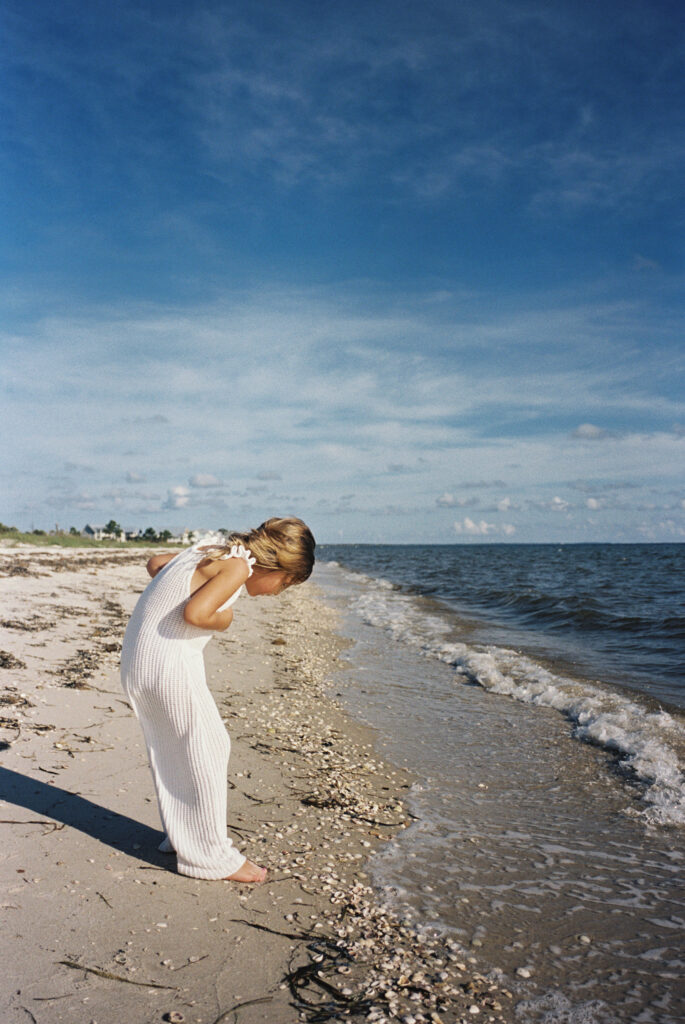 A little girl in white overalls collecting seashells along the forgotten coast of florida. 