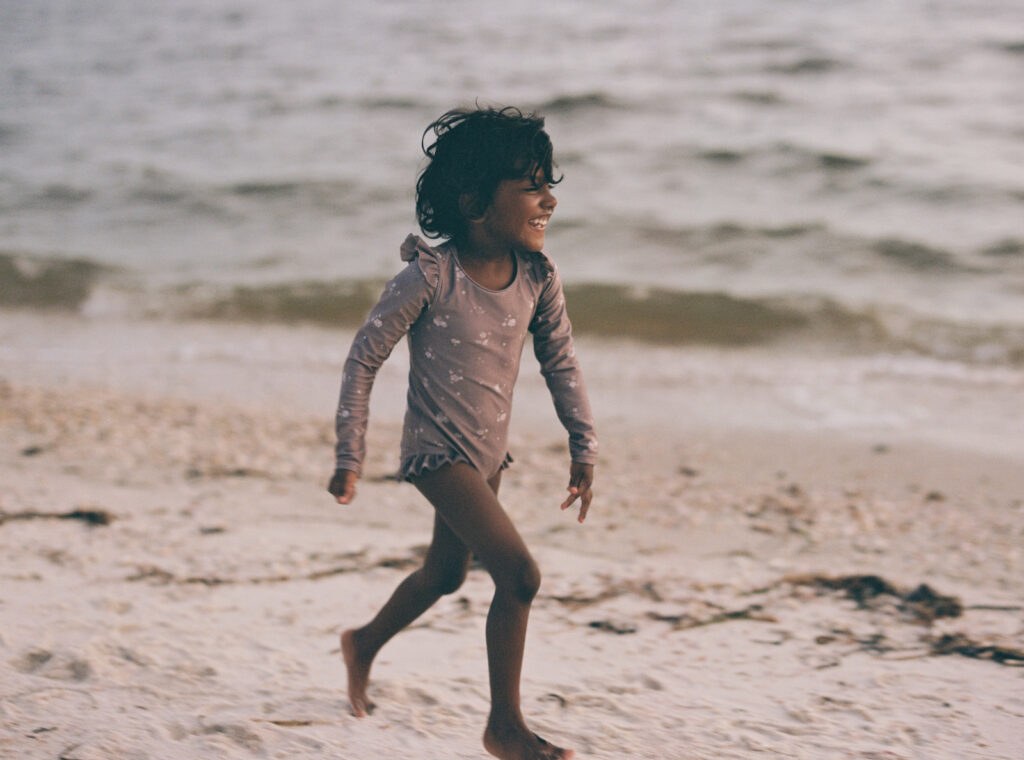 A little girl in a floral swimsuit runs along the shoreline of the forgotten coast of florida.