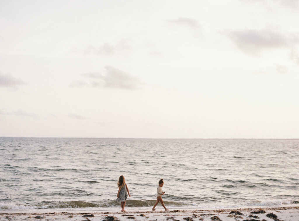 Two little girls collect seashells as the sun sets on the forgotten coast of florida. 