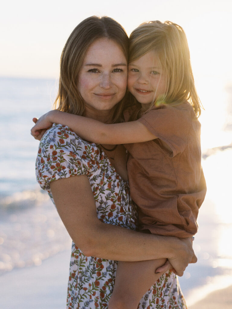 A mother in a beautiful floral dress holds her oldest daughter as they have a peaceful moment together in Miramar Beach, Florida. 