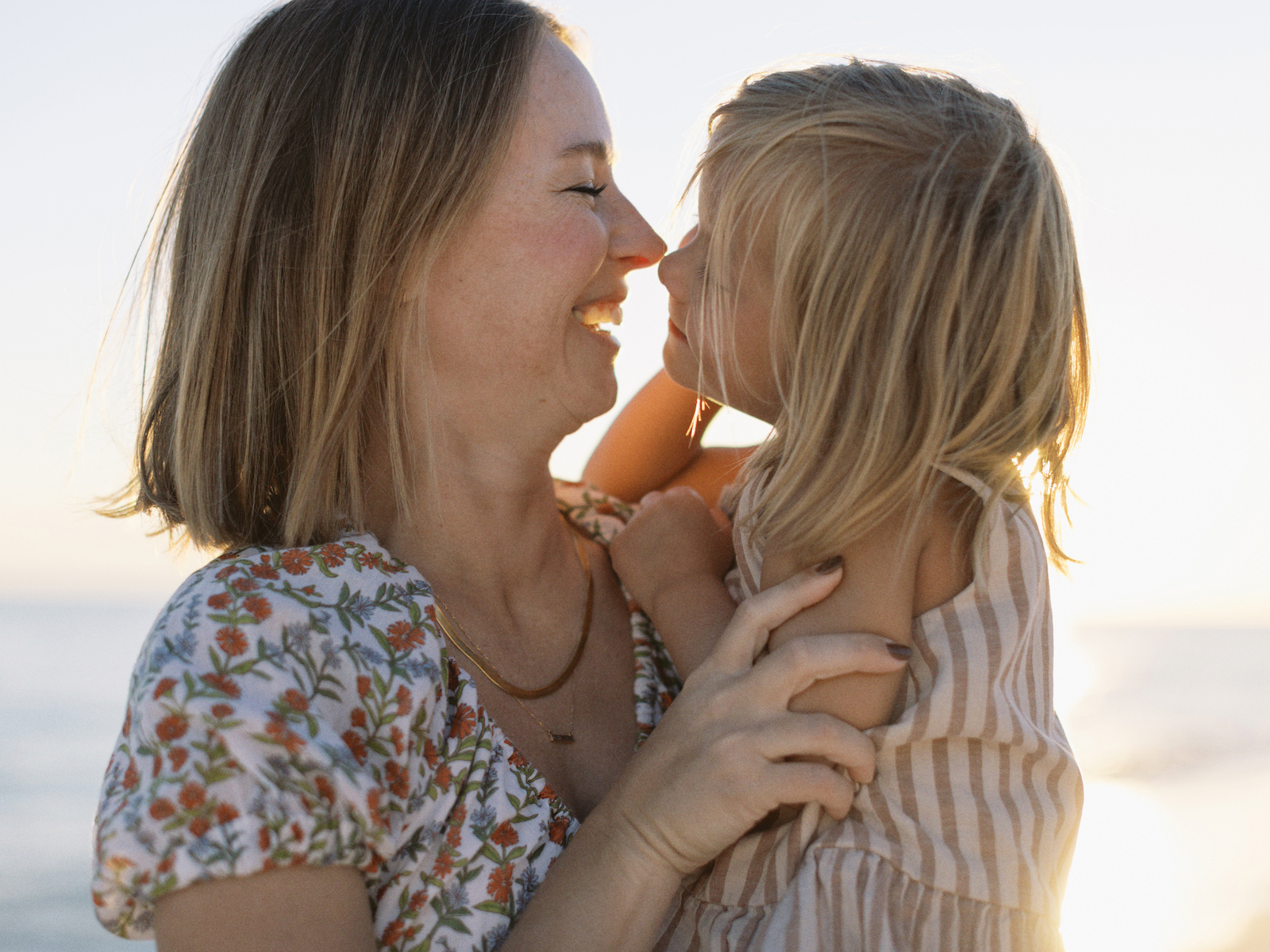A mother and daughter doing butterfly kisses on the nose while the sun sets behind them in Miramar Beach, Florida