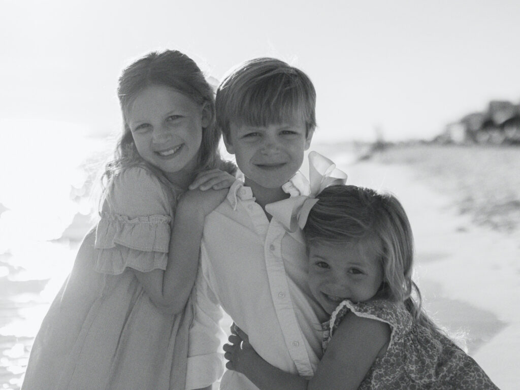 A boy and his two sisters hug each other tightly as they pose on the beach together in Destin, Florida. 