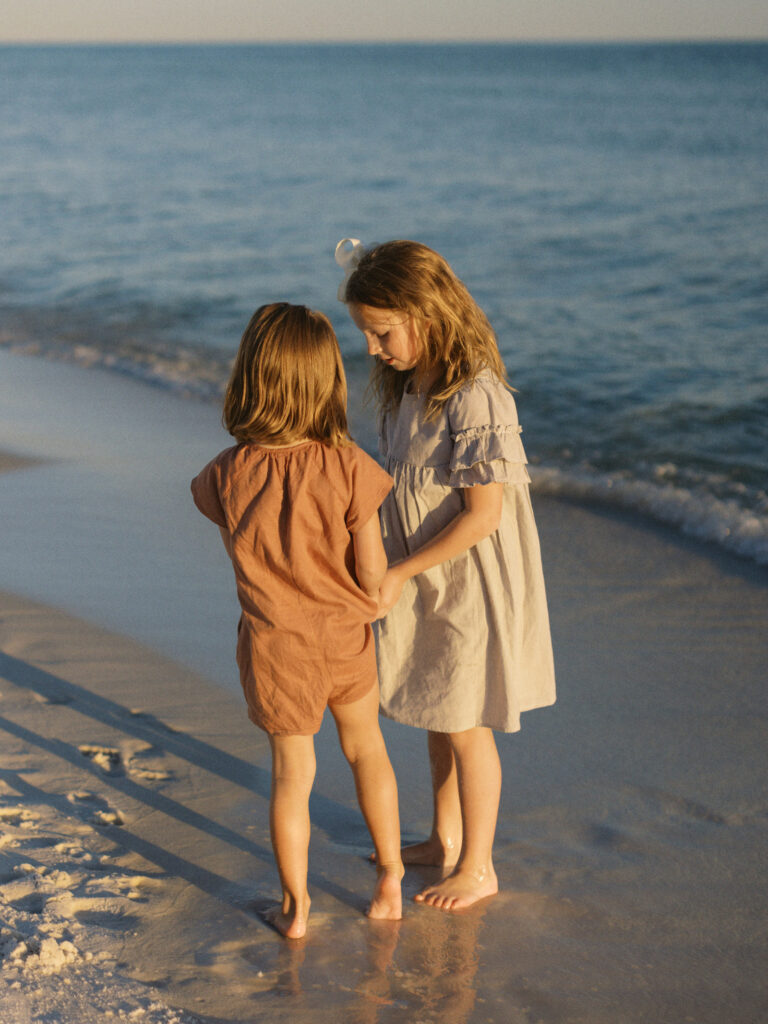 Two little girls share seashells on the beach in Destin, Florida. 