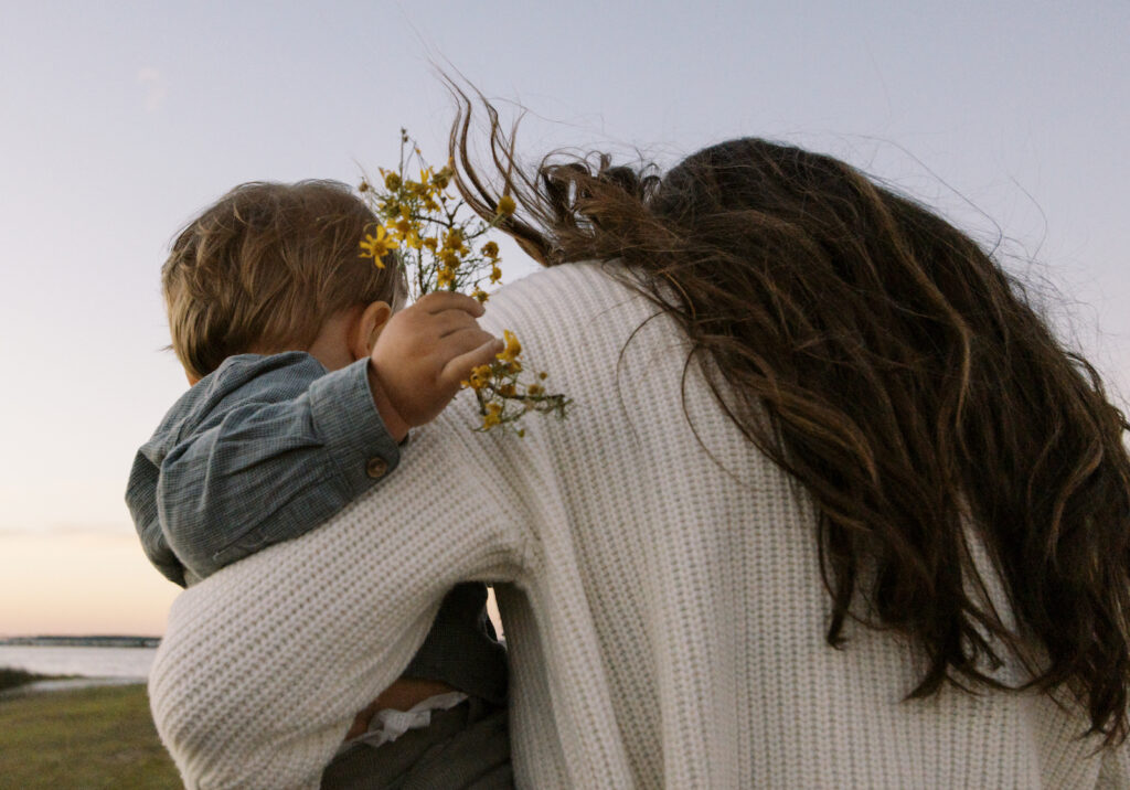 A mother holding her young son as he holds a bouquet of yellow wildflowers.