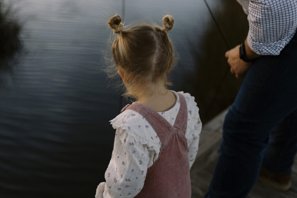 A young blonde girl with pig tails looking at a crap trap her father is pulling up over the dock.