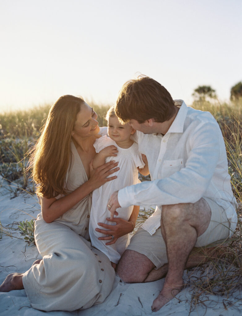 A mother and father cuddle their little daughter on the beach in 30A.