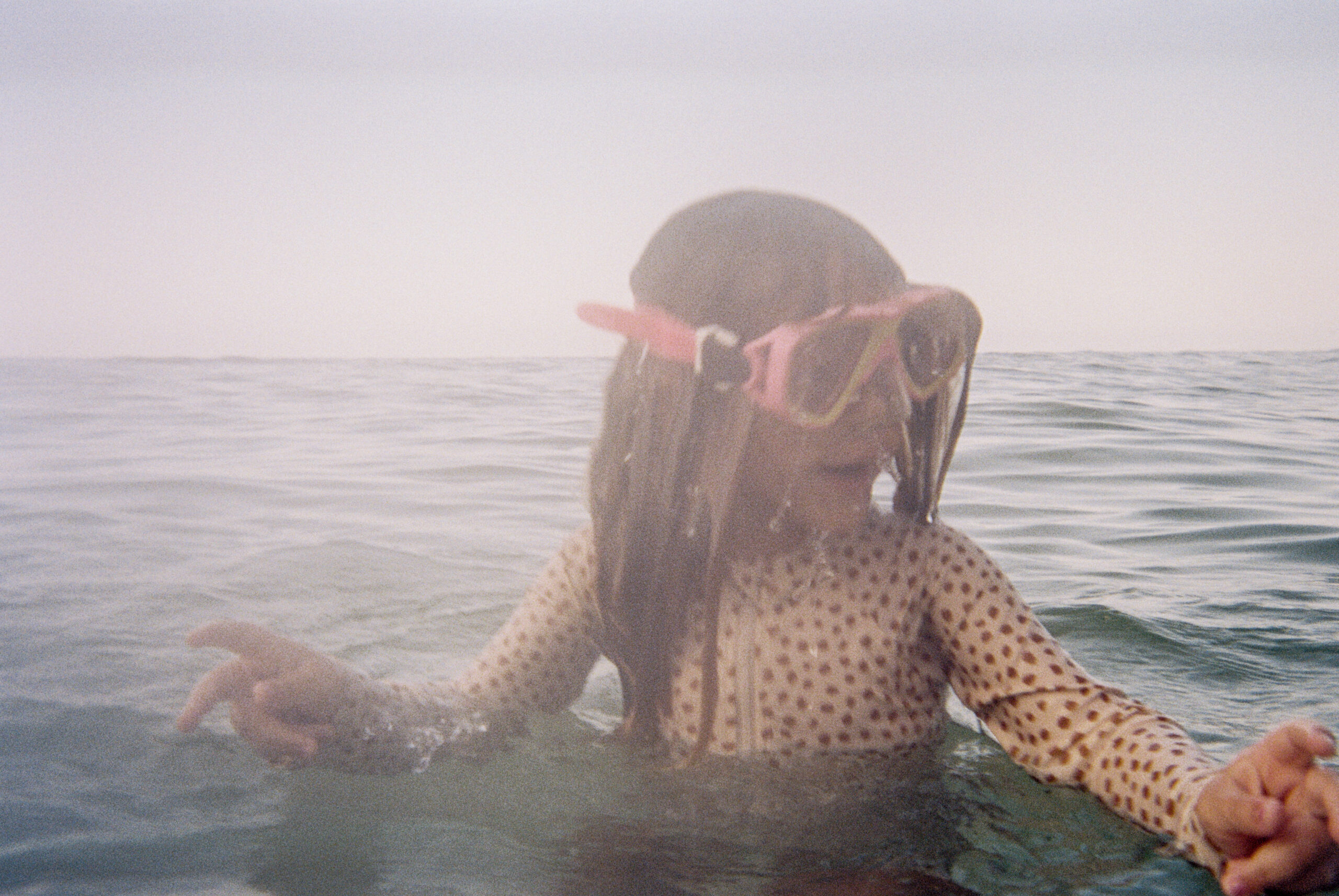 A little girl wearing pink snorkles rises up from the water while swimming in 30A Florida.