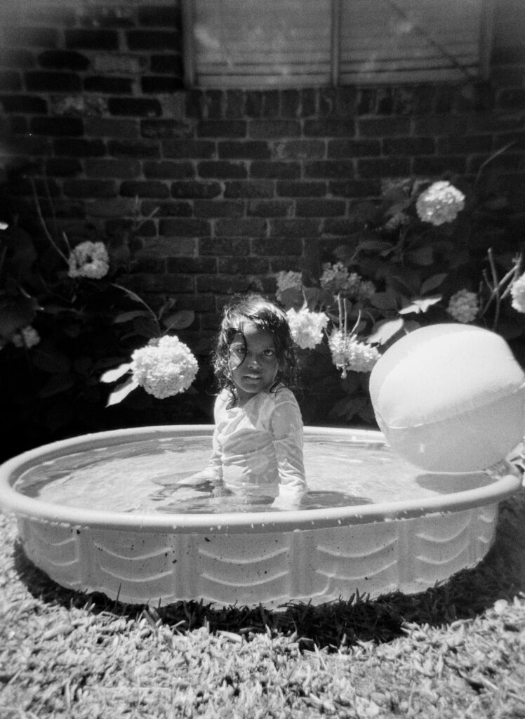 An Indian girl playing in the kid pool with a beach ball on a hot Summers day.