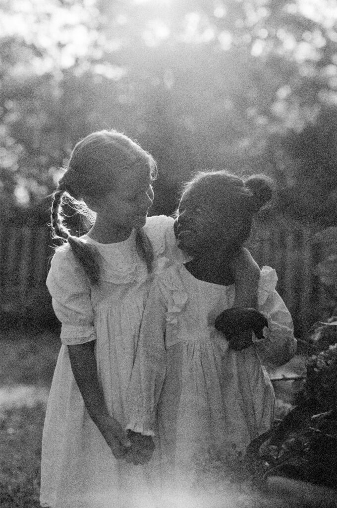 Two sisters through adoption smile at each other while standing in a garden.