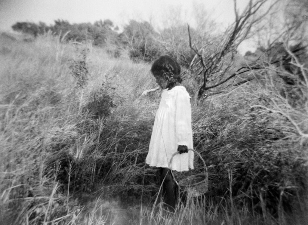 A little girl with a wicker basket searches for seashells in the marsh.