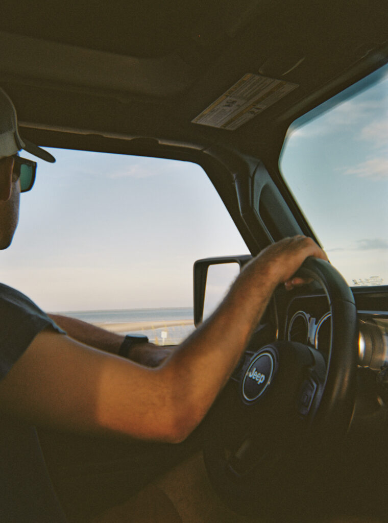 A man driving his jeep along the beach at sunset. 