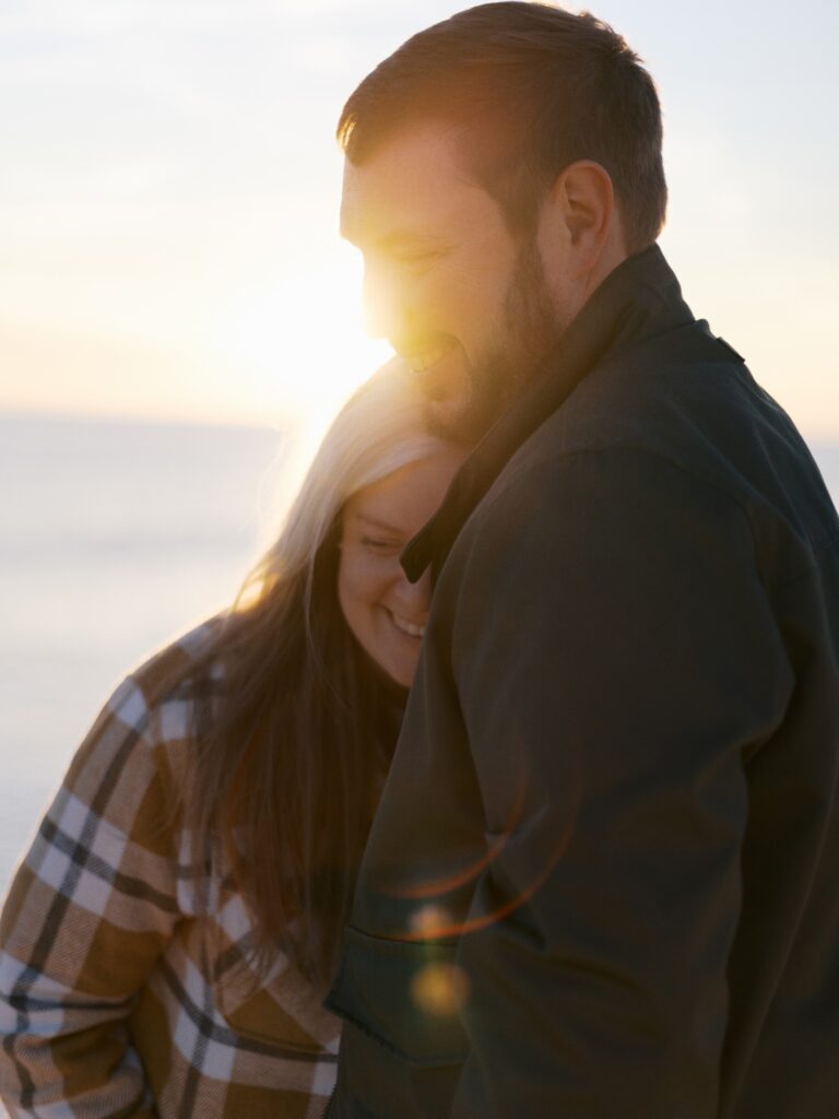 A couple huddles together to watch the sunset on the beach. 