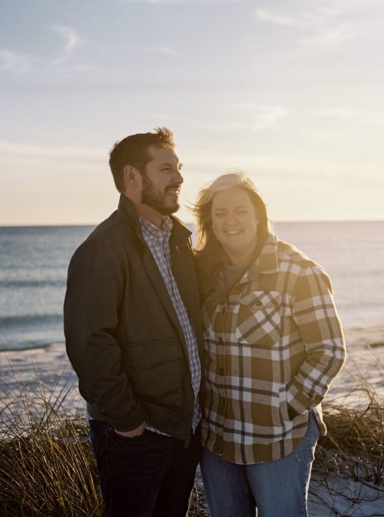 A couple laughs while hugging on the beach. 